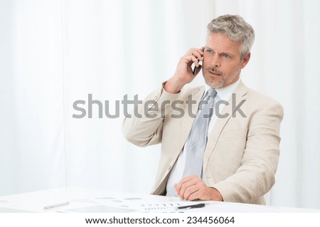 Mature Businessman Calling On Mobile Phone In Office