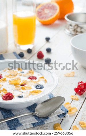 A glass of orange juice and a bowl of milk with cornflaks and fruit on a rusti table