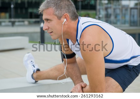 Mature Male Athlete Exercising And Listening To Music In The City