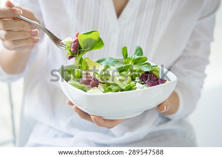 Close up shot of a woman holding a plate of fresh green salad in the beautiful morning light. She\'s holding a fork and she\'s about to eat the vegetarian food. Healthy eating and diet concept.