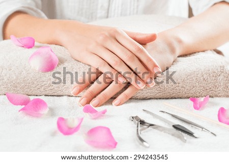 Closeup shot of female hands with french manicure on a towel surrounded by petals and manicure set. Woman getting nail manicure. Shallow depth of field with focus on woman hand.