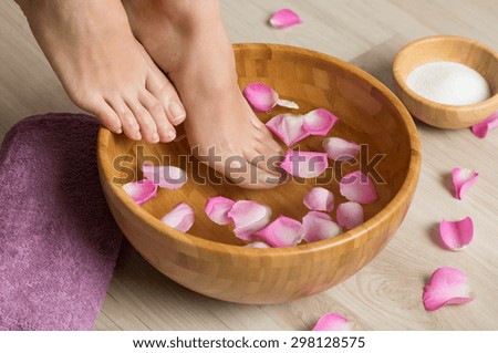 Closeup shot of a woman feet dipped in water with petals in a wooden bowl. Beautiful female feet at spa salon on pedicure procedure. Shallow depth of field with focus on feet.