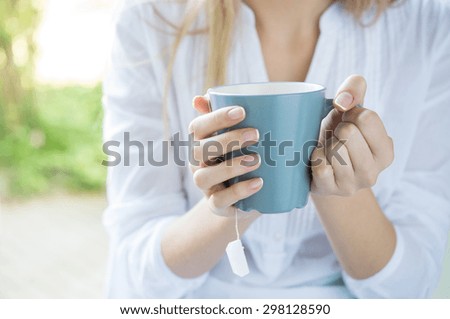 Closeup shot of a woman holding tea mug. Close up of young woman\'s hand holding a cup of hot tea. Relaxed girl drinking tea. Shallow depth of field with focus on tea mug.