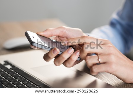 Closeup shot of a woman hand typing a text on mobile phone. Businesswoman holding a modern smart phone at office. Shallow depth of field with focus on cellphone.