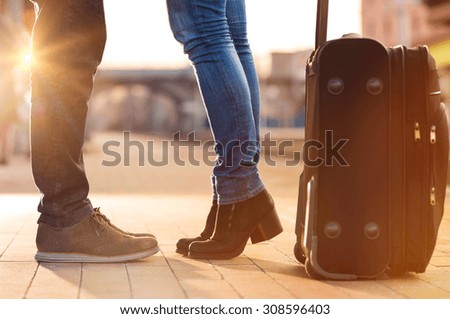 Closeup shot of woman feet standing on tiptoe while embracing her man at railway platform for a farewell before train departure. A travelling luggage is on the foreground.