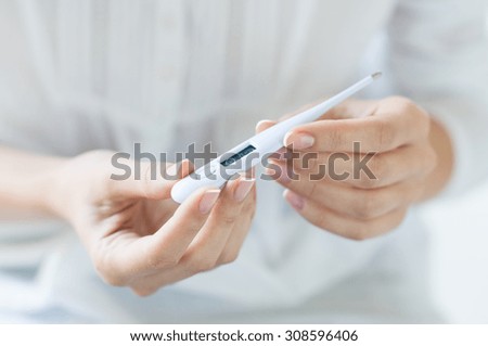 Closeup shot of a woman looking at thermometer. Female hands holding a digital thermometer. Girl measures the temperature. Shallow depth of field with focus on thermometer.