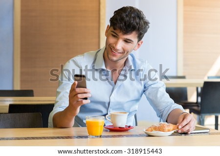 Closeup shot of man texting on mobilephone at cafÃ?Â?Ã?Â©. Guy is doing breakfast at coffee bar. Young man looking at smartphone and smiling during breakfast.