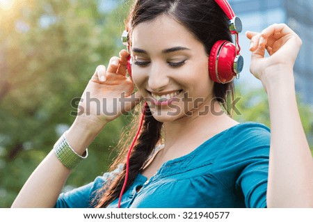 Closeup shot of young woman listening to music in a park. Portrait of happy smiling girl feeling free with music. Close up of latin girl listening to music with headphone and dancing in a city center.