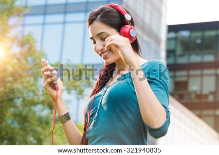 Closeup shot of young woman listening to music with mobile phone outdoor. Happy smiling girl listening to music with earphone. Portrait of carefree woman listening to music in a city center.