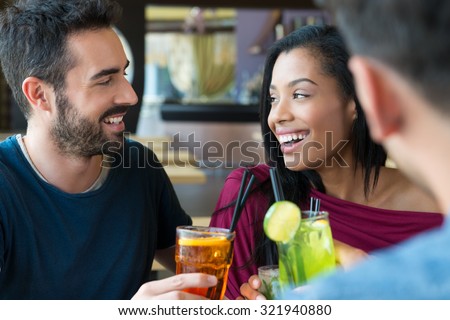 Portrait of happy young man and woman holding cocktail glasses. Friends drinking an alcoholic beverages at bar. Smiling young man and woman drinking juice and smiling. Aperitif time.