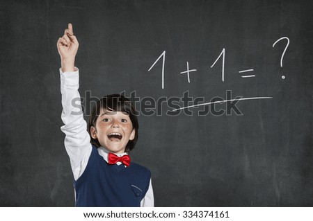 Little scholar boy knows the solution of this easy problem. Schoolboy pointing high his index finger. Cheerful cute boy with raised hand standing against black background.