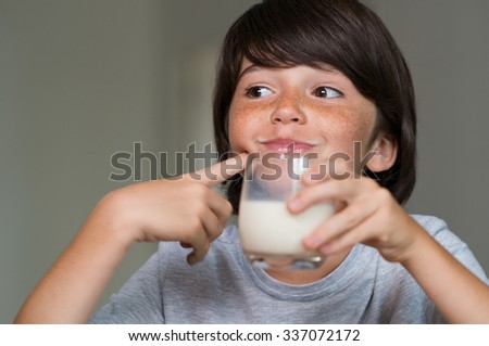 Closeup of little boy drinking glass of milk. Happy kid smiling and drinking milk indoor. Smiling cute boy drinking glass of milk for breakfast.