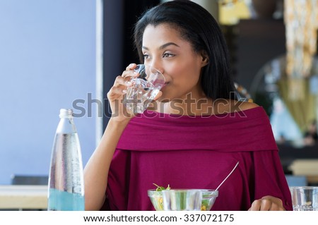 Closeup shot of young woman drinking a glass of water. African girl drinking water durinh her lunch break at restaurant. a Beautiful girl thirsty drink a glass of water and looking away.
