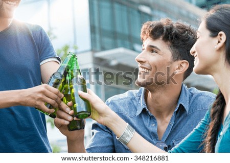 Closeup shot of young friends toasting with bottles of beer. happy smiling guys and women drinking beer outdoor. Carefree group of people cheers with beer at sunset.
