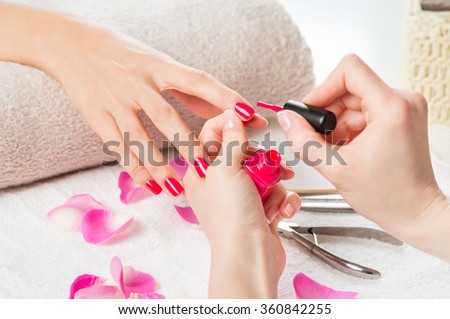 Closeup shot of a beautician applying nail polish to female nail in a nail salon. Close up of a woman hand with pink nailpolish after the manicure.