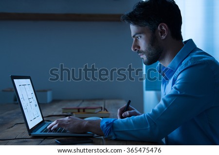 Architect sitting at night working on architectural plan on laptop. Young interior designer in casual checking blueprint of a house on laptop. Architect studying the map and layout of a new project.