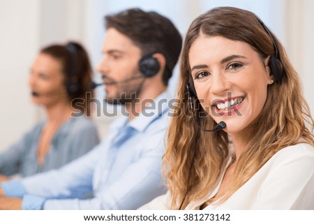 Smiling female call centre operator doing her job with a headset while looking at camera. Portrait of happy woman in a callcenter smiling and working. Portrait of happy smiling support phone operator.