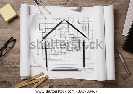 Top view of architectural blueprints, rolls and drawing instruments on the worktable. Shape of house with black pencils on a project house. Architectural drawings with house keys, new home concept.