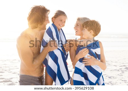 Wet son and daughter draped in towel embracing by parents after swim. Happy family at beach after swim in the tropical sea. Smiling father and mother drying children with a towels.