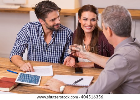 Young happy couple receiving house keys from real estate agent. Giving keys of new house to young couple. Smiling couple signing financial contract for mortgage.