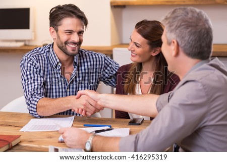 Handshake of a mature manager with a happy young couple at office. Businessmen handshake during meeting signing agreement. Happy man shaking hands whit his finacial advisor.