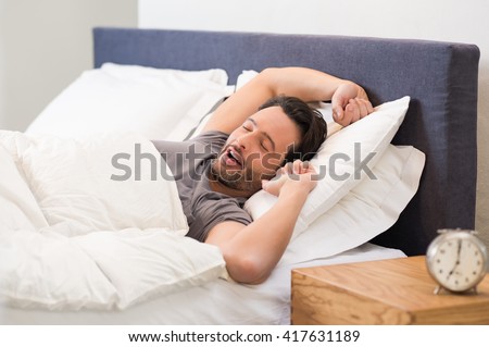 Young man stretching while waking up in the morning. Man yawning while waking up. Lazy young man in sleep. Portrait of latin man yawns and stretches in bed.