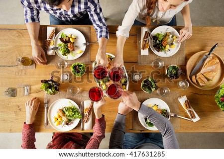 Top view of group of friends raising a toast post lunch. High angle view of happy men and women celebrating at home with red wine. Close up shot of friends toasting glasses of red wine in a party.