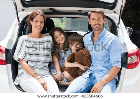 Family car trip on summer vacation. Happy smiling parents and two children in car having fun. Cute small boy holding teddy bear sitting with sister and parents in car for road trip with car.