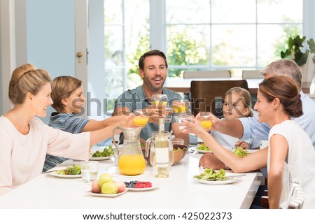 Smiling generation family raising glasses together in the kitchen. Happy parents with children and grandparents celebrating with a toast. Cheerful family raising toast with juice at dining table.