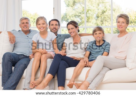 Portrait of happy family sitting on couch at home. Smiling parents, grandparents and happy children looking at camera. Portrait of extended family group sitting together.