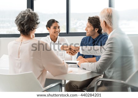 Handshake to seal a deal after a job recruitment meeting. Two business people shaking hands in front of their colleagues. Senior businessman shaking hands to young businesswoman in a modern office.