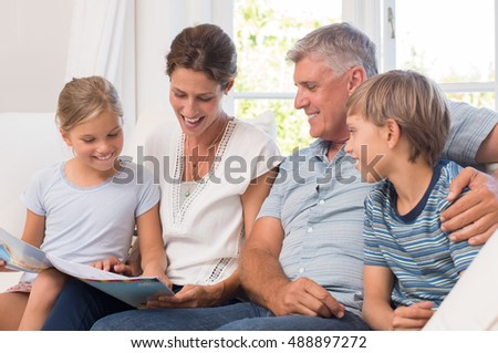 Young girl showing her coloring book to mother and grandfather. Grandfather visiting grandchildren enjoying. Happy mother sitting on couch with her children and grandpa.