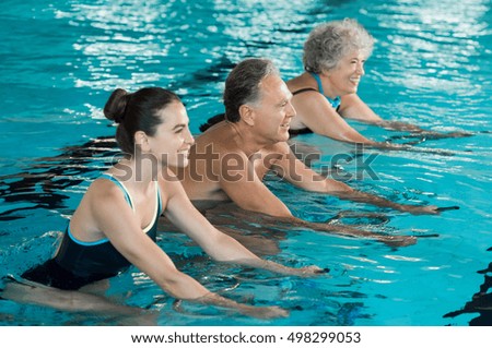 Happy smiling mature man and old woman cycling on a water bike in swimming pool. Happy and healthy senior people doing aqua aerobics on exercise bikes in a swimming pool. Fitness class training.