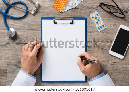 High angle view of doctor hand writing prescription on paper. Top view of hand of doctor writing on white blank paper with medicine and capsule on a wooden table. Health and medical concept.