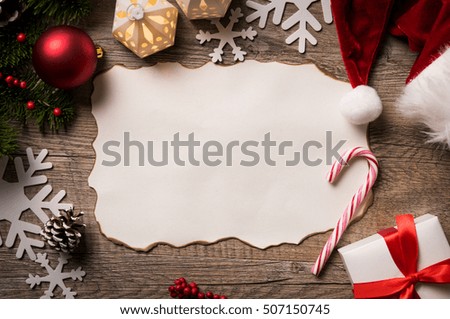 High angle view of empty letter on wooden table with christmas decoration. Top view of empty xmas wish list with little gift present and santa claus hat on wooden background.