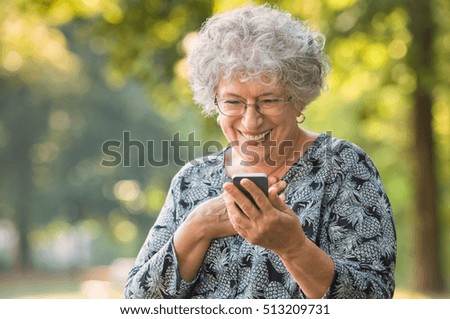 Cheerful old woman excited on receiving some good news over smartphone. Happy senior woman at park using mobile phone. Cute elderly woman receive a message phone for her beloved.