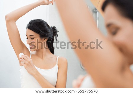 Woman applying deodorant on armpit in bathroom. Beautiful young woman putting antiperspirant stick in underarms. Smiling girl applying stick in deodorant armpit.