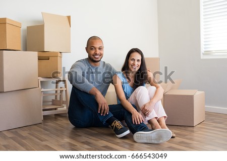 Young multiethnic couple with piles of cardboard boxes after buying a new apartment. African man embrace his smiling girlfriend sitting on floor in their new home. Real estate and loan concept.