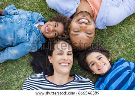 Overhead view of cheerful family lying on grass in a circle and looking at camera. High view of multiethnic family lying at park. African father and hispanic mother with their smiling children.