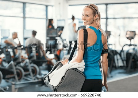 Fit woman holding gym bag in a fitness centre. Beautiful blonde woman ready to start her training. Portrait of energetic woman looking at camera ready for new inscription at the gym.