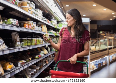 Young woman shopping in grocery store. Mature woman checking food label in supermarket. Latin woman holding shopping basket and choose a product in supermarket.