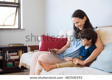 Mother and son sitting on sofa using digital tablet. Happy mom and little boy using tablet with touchscreen together watching a video. Smiling mother and cute boy playing on digital tablet.