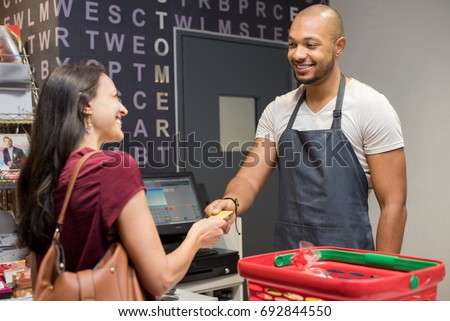Happy woman at checkout of grocery store paying with credit card to cashier. Smiling woman paying with her EC card at supermarket. Mature woman at cash register paying with credit card to man.