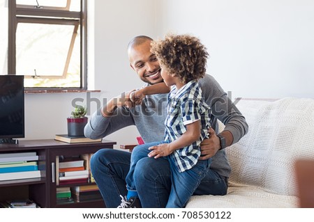 Happy african father and son punching knuckles. Young black man and little boy playing with each other at home in living room. Happy dad and smiling child playing by punch their fists.