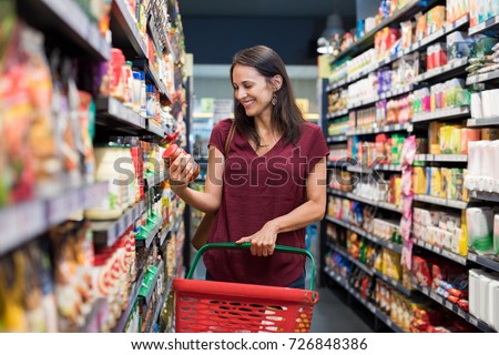 Happy mature woman looking at product at grocery store. Smiling hispanic woman shopping in supermarket and reading product information. Costumer buying food at the market.