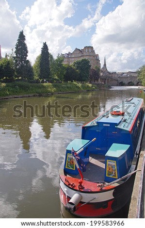 A colorful boat on the river Avon in Bath and in the background the Pulteney Bridge that crosses the river