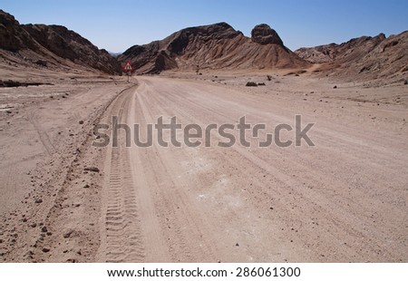 Gravel road in the center of Namibia running through desert and a dry landscape with small Mountains in the background