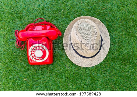 Old red phone with hat on the field of green grass, communication vintage style