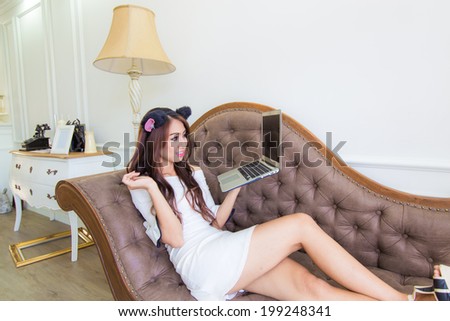 Smiling asian young sexy woman using laptop while relaxing on sofa at home, fashion portrait women