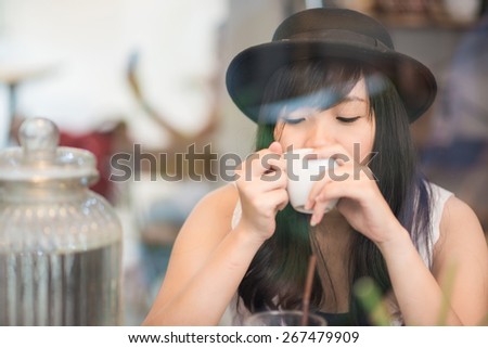 Young asian woman drinking coffee through the mirror in a trendy vintage cafe